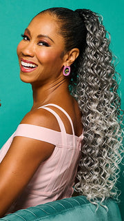 Model is wearing 27" GLAM CURLS PONY by KIM KIMBLE in color MC511SS POWDERED LICORICE | Dark Grey with Light Grey Highlights